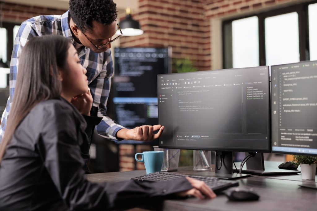 Two developers discussing a software project on a computer in a development agency office